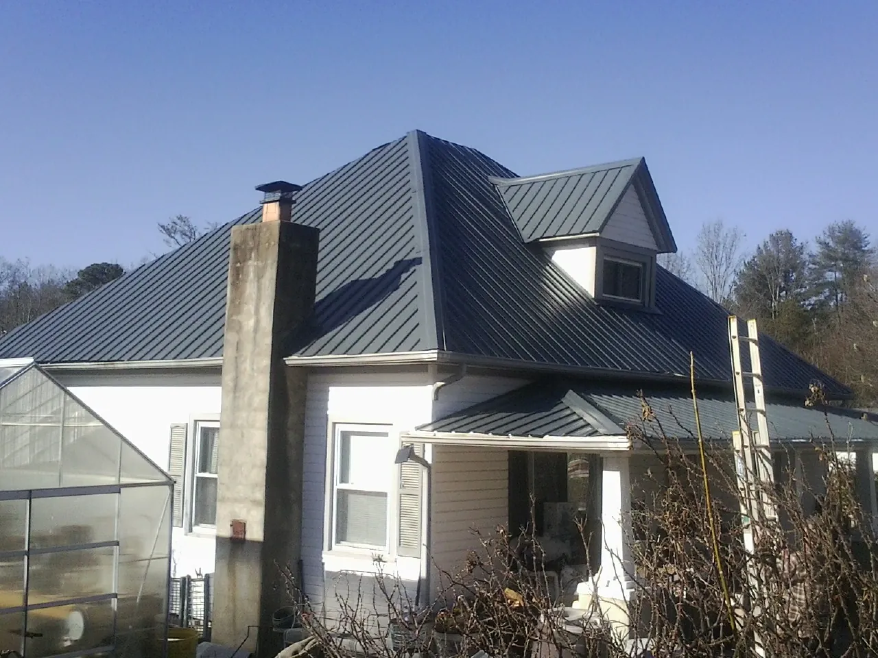 Dark blue standing seam metal roof on a white farmhouse with dormer — Slate & Tile Roof Repair by Roofing Brothers in Bloomdale
