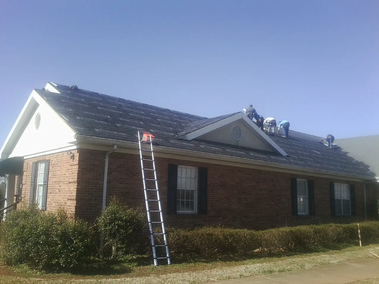 Crew tearing shingles off a brick ranch roof with a ladder set — Metal Roof Repair work by our crew in Bloomdale