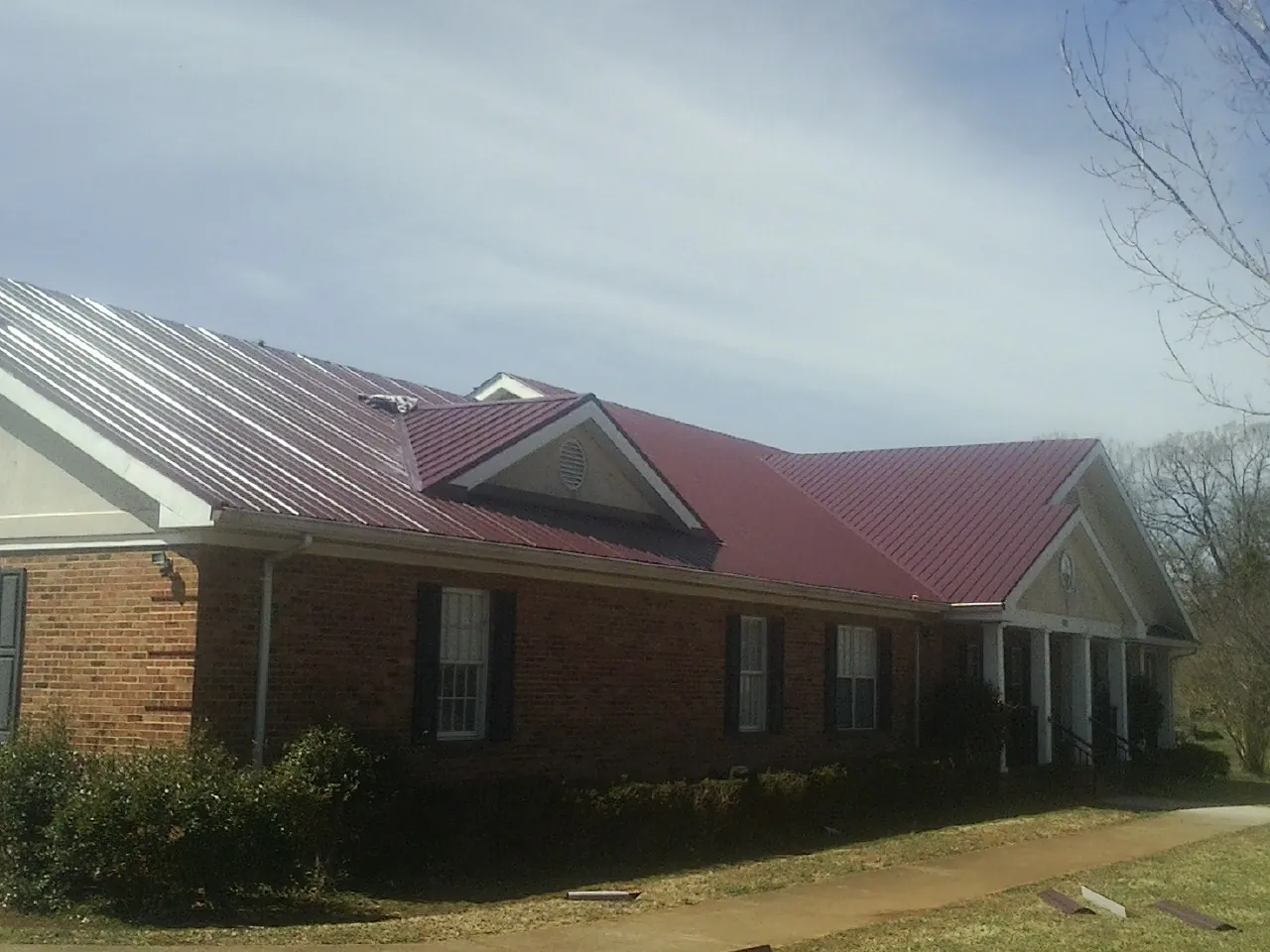 Red metal roof with gabled entries on a long brick building, from a Hail Damage Roof Repair job in Bloomdale