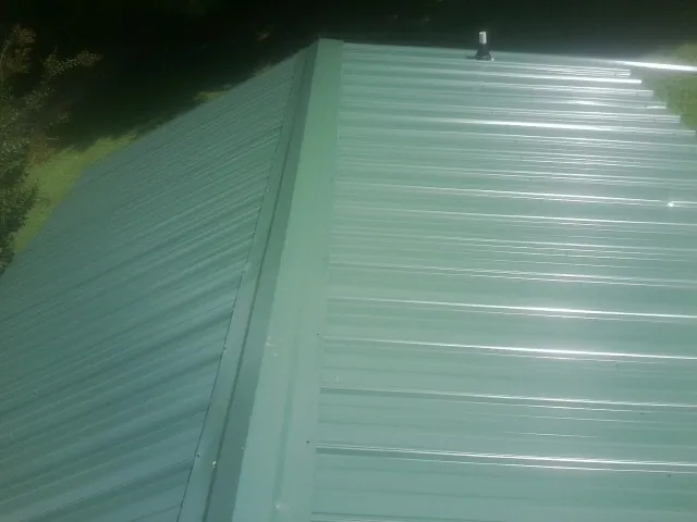 New green metal panels meeting at the ridge of a roof — Flat Roof Repair work by our crew in Bloomdale