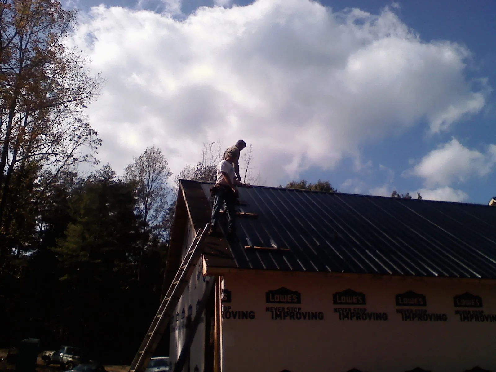 Roofer fastening dark metal panels high against a cloudy sky, from a Roof Inspection job in Bloomdale