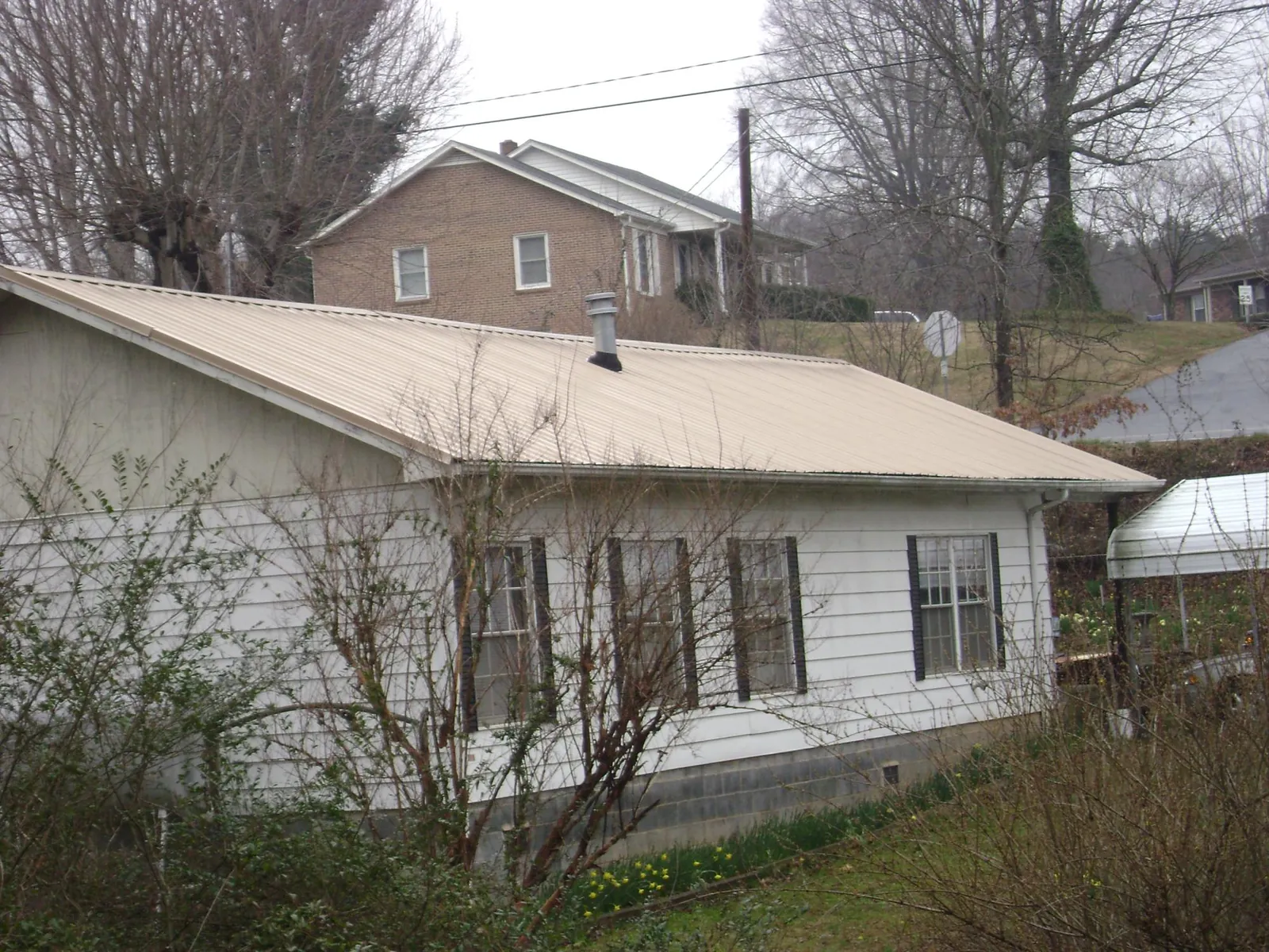 Tan metal roof on a white sided house set into a hillside — Commercial Roofing by Roofing Brothers in Bloomdale