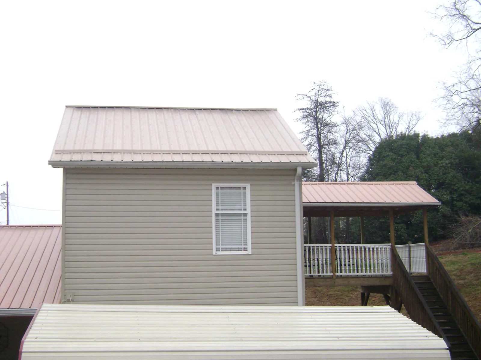 Tan metal roofs on a two story addition and attached porch, from a Roof Replacement job in Bloomdale